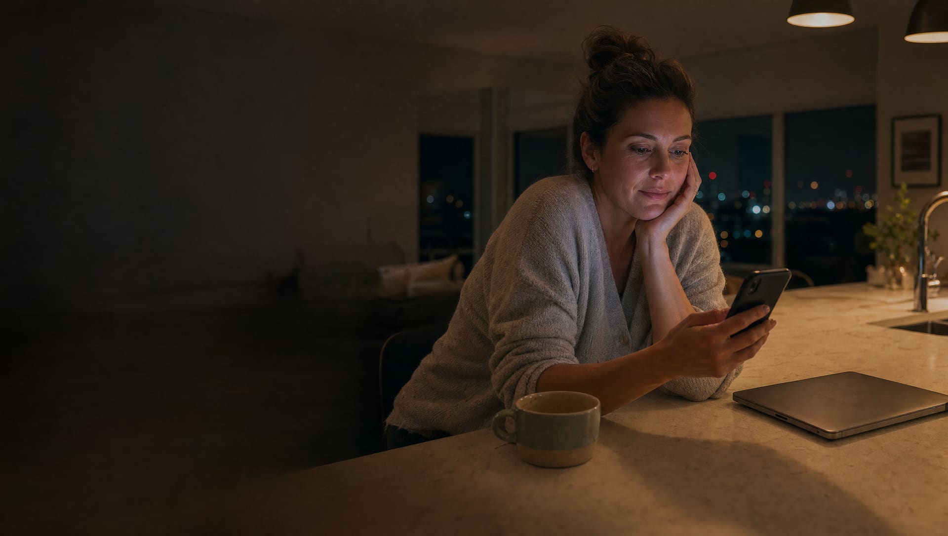 A woman at her kitchen bench late in the evening, weighing up a property on her phone