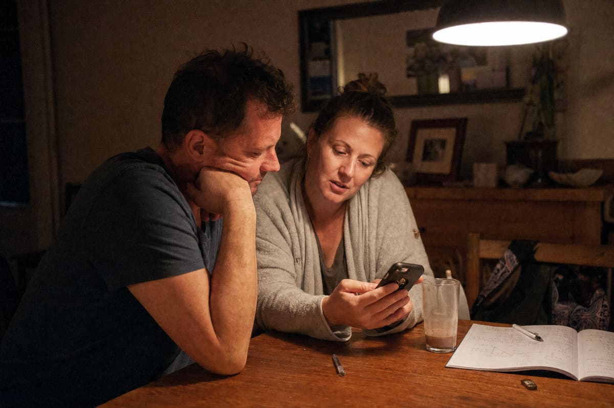 A couple in their forties talking over one phone at their dining table late at night
