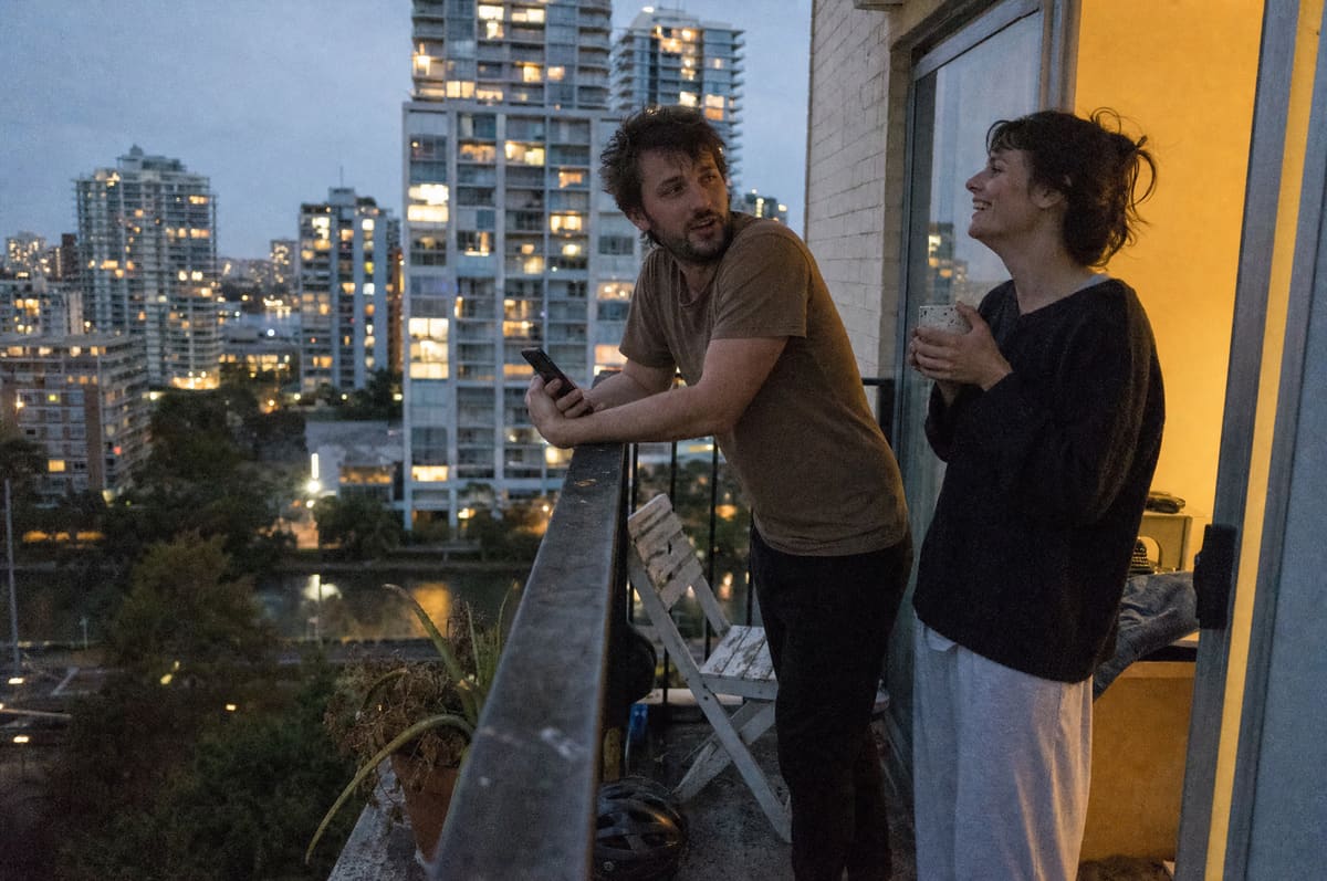 A young couple on their rented apartment balcony at dusk, city skyline in the distance
